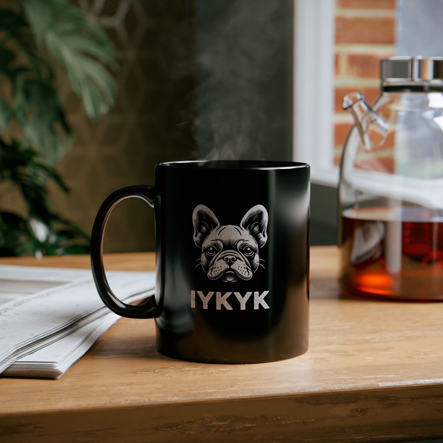 Black ceramic mug with white portrait of a French Bulldog and the slogan "IYKYK" on wood counter